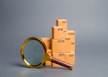 A pile of boxes and a magnifying glass. Concept search for goods and services. Tracking parcels. Quality control. Search for customers. Network monitoring system for the best supply of goods