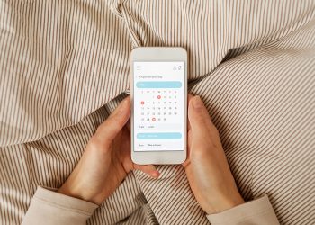 Close-up of woman holding mobile phone and planning her day with calendar